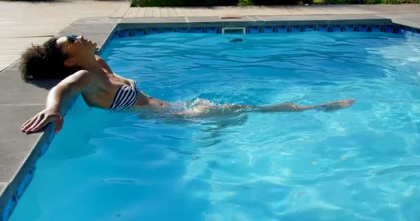 年轻的混血女子在游泳池里放松的侧视图 她在4K 游泳馆里晃动着腿 — 图库视频影像