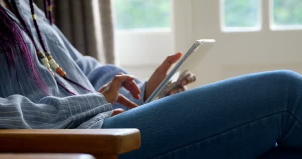 デジタル タブレットを使用して快適な家のリビング ルームで若い黒人女性の中間セクション 彼女は彼のソファの上に座って デジタル タブレット 上のスクロール — ストック動画