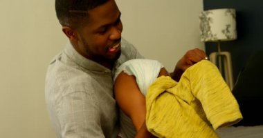 Genç siyah babası oğlunun giysilerini yatakta rahat bir ev değiştirme yardımcı yan görünüm. O gülümseyen ve oğlu 4 k tutan