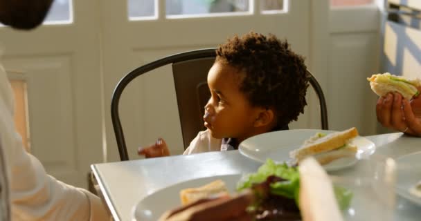 快適な家のキッチンでダイニング テーブルで食事はかわいい黒息子の正面 サンドイッチ を餌の母 — ストック動画