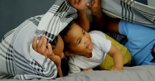 快適な家のベッドの上の息子と遊ぶ若い黒親のフロント ビュー 彼らは の毛布の下に隠れています — ストック動画