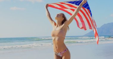 Bir Amerikan bayrağı sahilde tutan genç Kafkas kadın önden görünümü. Amerikan bayrağı elinde 4 k çırpınan