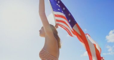 Bir Amerikan bayrağı sahilde tutan genç Kafkas kadın yan görünüm. Amerikan bayrağı elinde 4 k çırpınan