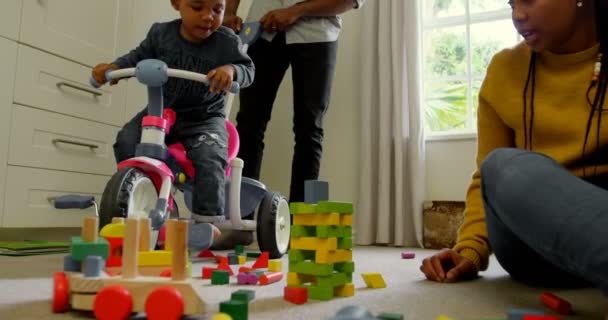 年轻的黑人父亲教儿子在舒适的家里骑三轮车的低角度 母亲坐在地板上看着玩具4K — 图库视频影像