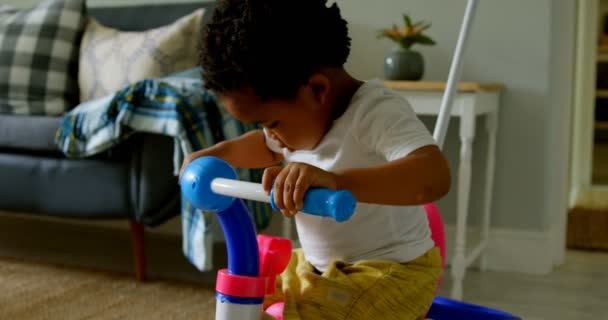 快適な家で遊ぶかわいい小さな黒人の男の子の側面図です 三輪車 に座ってる — ストック動画