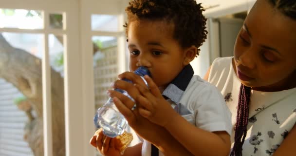 Vista Lateral Joven Madre Negra Alimentando Con Agua Hijo Cocina — Vídeo de stock