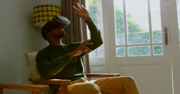 快適な家の仮想現実のヘッドセットを使用して若い黒人男性のフロント ビュー 彼は身振りで示すことは の椅子に座って — ストック動画