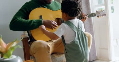 Önden Görünüm genç siyah baba ve küçük oğlu oturma odasında rahat ev gitar çalmak. Gitar el 4 k ile isabet oğlu