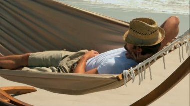 Beyaz adam sahilde bir hamakta uyumak yan görünüm. Yüzünde 4 k ile şapka rahatlatıcı