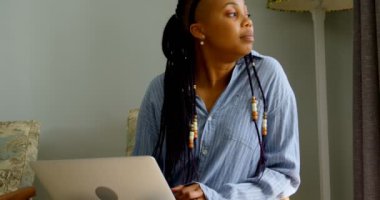 Dijital tablet kullanma ve rahat ev içinde kanepede oturan genç siyah kadın yan görünüm. 4 k bakıyor