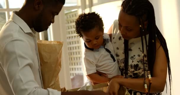 前面的看法年轻的黑人母亲和儿子看在厨房舒适的家购物袋 父亲拿着购物袋4K — 图库视频影像