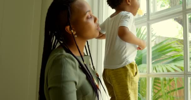 快適な家の窓枠に息子と遊ぶ若い母親が黒の側面図です 彼らは の窓から外を見てください — ストック動画