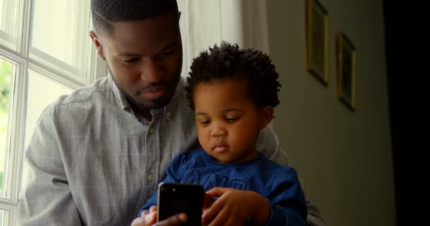 Πρόσοψη Μαύρη Πατέρα Και Γιου Χρησιμοποιώντας Smartphone Ένα Άνετο Σπίτι — Αρχείο Βίντεο