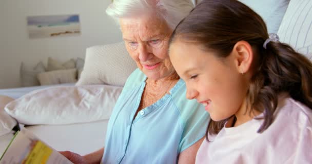 白种人外婆和孙女在舒适的家中看书的侧视图 他们面带微笑 看着书4K — 图库视频影像