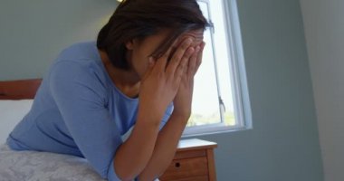 Olgun kadın yatakta rahat ev alnından üzerinde el ile oturuyordu yan görünüm. O üzgün ve stresli. 4k