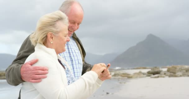 ビーチでの携帯電話で古い白人の年配のカップル撮影 Selfie の側面図です 彼らは笑みを浮かべて のビーチで楽しんで — ストック動画