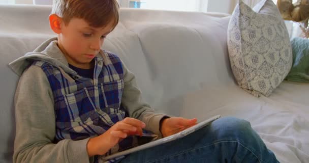 デジタル タブレットの快適な家を訴える白人少年の正面 のソファに座っています — ストック動画