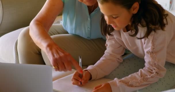 正面の古い白人の祖母の家での宿題を自分の孫娘を助けます 自分の書いているノート — ストック動画