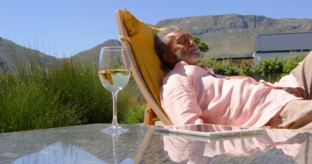 在家里后院的泳池甲板椅子上放松的老黑人的侧视图 表4K 上的葡萄酒玻璃和数字平板电脑 — 图库视频影像