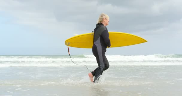 Eski Beyaz Kadın Surfboard Ile Plajda Çalışan Kıdemli Yan Görünüm — Stok video