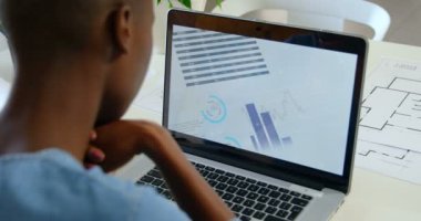 Masada oturan ve modern ofis içinde laptop üzerinde çalışan genç siyah iş kadını arkadan görünüş. Dizüstü bilgisayar ekranında 4 k çalıştıran grafikler