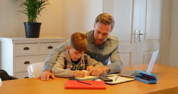 快適な家のテーブルで宿題で息子を助ける若い白人父のフロント ビュー のラップトップを使用しています — ストック動画