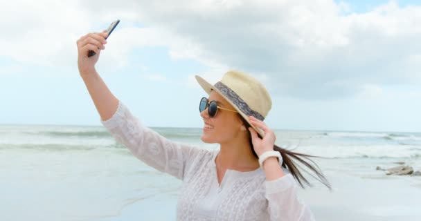 ビーチでの携帯電話で Selfie を取っての若い白人女性の側面図です 彼女はポーズと笑顔 — ストック動画