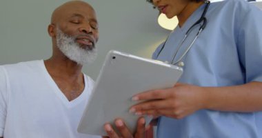 Tıbbi raporlar evde olgun adamla tartışırken genç karışık ırk doktor düşük açılı görünümü. O dijital tablet 4 k kullanıyor