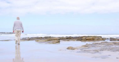 Dikiz kumsalda yürüyen eski beyaz üst düzey adam. Güzel gök ve 4k planda sakin deniz