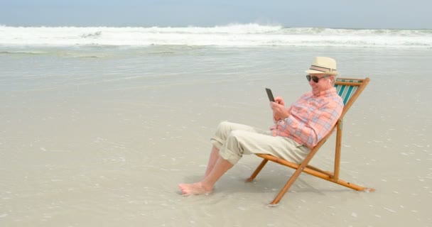 ビーチでの携帯電話で Selfie を取って古い白人の年配の男性の側面図です 彼はビーチ でサンラウンジャーでリラックス — ストック動画