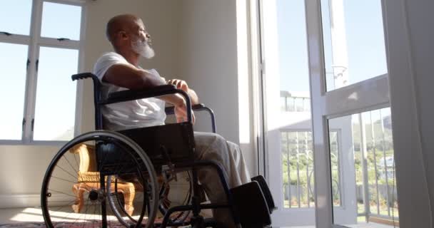 在家里的窗户附近坐在轮椅上的成熟的黑人残疾人的侧视图 他在思考 从4K 窗口看 — 图库视频影像