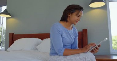 Olgun kadın yatakta rahat bir ev üzerinde dijital tablet kullanarak yan görünüm. Gülümseyen kadın 4 k dijital tablete yazma