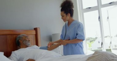Evde yatakta komuta sizde kan basıncı kontrol karışık ırk genç kadın doktor önden görünümü. O stetoskop 4 k kullanıyor