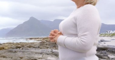 Eski beyaz kadın kumsalda sıktı elleri ile ayakta kıdemli yan görünüm. O gülümseyen ve Dış Saha 4 k arıyorsunuz