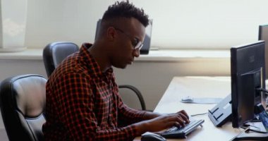 Modern bir ofis masasında çalışan genç siyah işadamı yan görünüm. Okul sırası pc 4 k kullanıyor