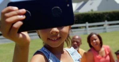 Sevimli küçük siyah kız parkta cep telefonunda selfie tıklayarak aile ile önden görünümü. Gülümseyen ve 4 k poz