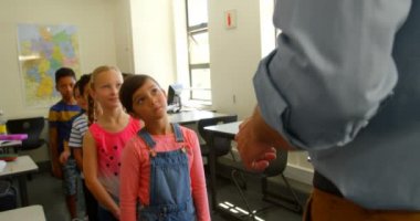 Yetişkin beyaz erkek öğretmen okulda bir sınıfta okul öğrencileri arka görünümü. Bir satırda 4k ayakta okul çocukları