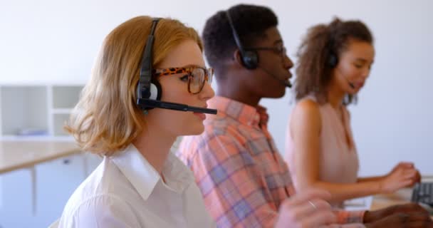 現代のオフィスでヘッドセットで話している若い多民族顧客のセールスエグゼクティブの側面図 机で一緒に働いている — ストック動画