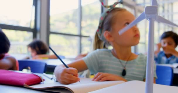在教室里的课桌上学习的高加索女学生的前面 教室书桌上的风力涡轮机模型 — 图库视频影像