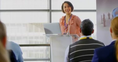 Onu laptop ile podyum üzerinde duran ve bir iş Semineri 4 k halka konuşma Asyalı bir kadın konuşmacı önden görünümü