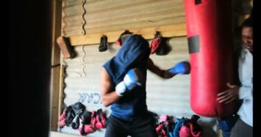 Genç Afro-Amerikan erkek boksör boks eğitmen fitness salonunda ile pratik yan görünüm. O kum torbası 4 k vuruyor