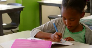 Okulda sınıfta masada okuyan sevimli Afro-Amerikan kız öğrencinin ön görünümü. Not defterine çiziyor. 