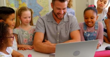 Okulda sınıfta dizüstü genç Kafkas erkek öğretmen öğretim okul çocukları ön görünümü. Onlar görünümlü ve 4k gülümseyen