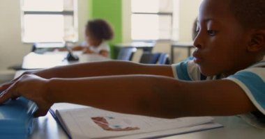 Sınıfta masa başında otururken okuyan sevimli Afro-Amerikan öğrencinin yan görünümü. Kalem kutusunu 4k açıyor.