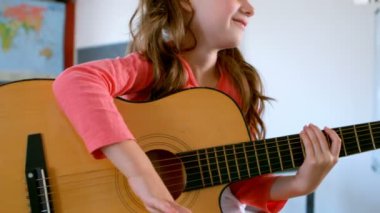 Masada oturan ve bir sınıfta gitar çalmak sevimli beyaz kız öğrenci orta bölümü. 4 k gülümsüyor