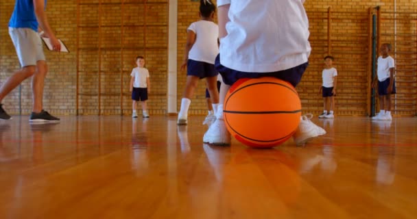 白人女子高生学校でバスケット ボールのコートでバスケット ボールの上に座っての低部は 学童バック グラウンド でバスケの練習 — ストック動画