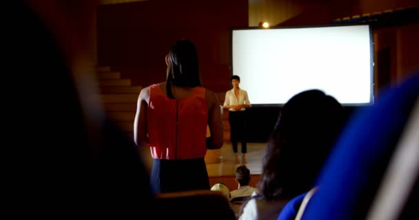 講堂でのセミナー中にアジアの女性スピーカーに質問する若いビジネスウーマンの背面図 彼女に答える女性スピーカー — ストック動画