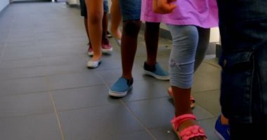 Okulun koridorunda bir sırada yürüyen okul çocuklarının düşük bölümü. 4k birlikte oynuyorlar