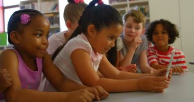 Masada dijital tablet üzerinde birlikte okuyan okul çocukları çeşitli grubun yan görünümü. Dijital tablet 4k kullanırken gülümsüyorlar