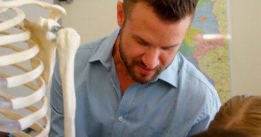 Okulda sınıfta insan iskeleti modelini tamir yetişkin Kafkas erkek öğretmenin ön görünümü. Okul çocukları ona 4k yardım